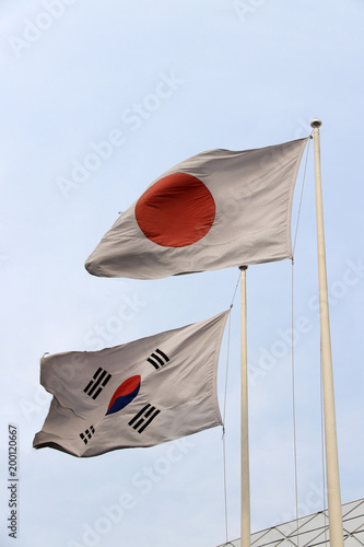 The flag of Japan and Republic of Korea on blue sky background, Red circle on the white in Japanese and a red with blue Taeguk, symbolizing balance, in its center, and four black trigrams in Korean.