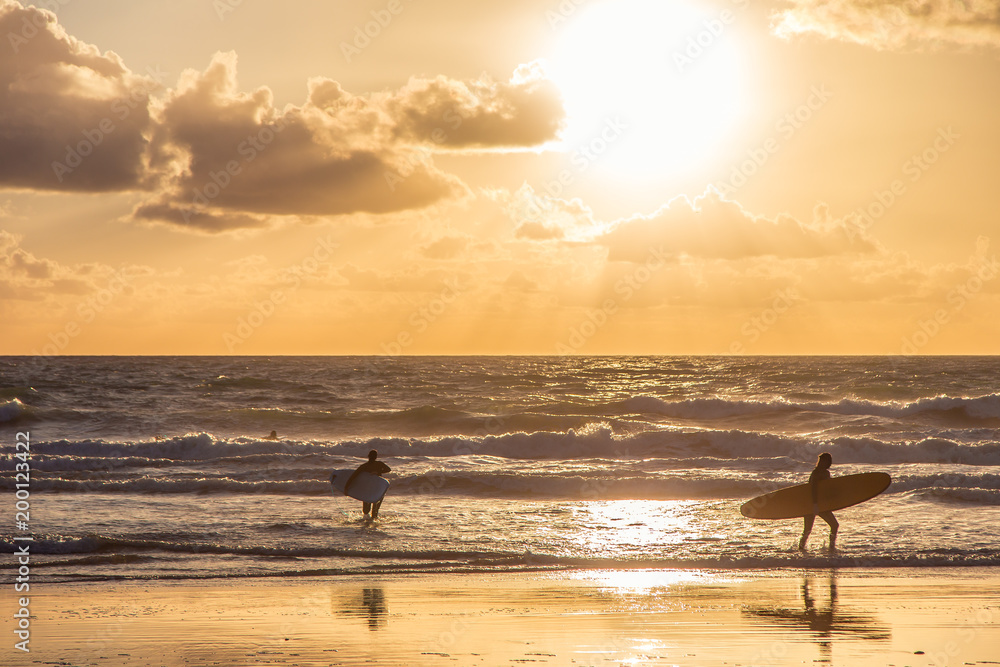 Surfers in the beach under a beautiful cloudy sky at the sunset