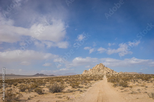 Long sandy dirt road leads down to a hill made of rock boulders.
