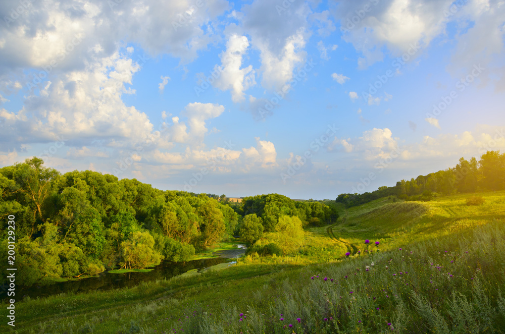 Sunny summer landscape with river at sunrise.Green hills with trees.