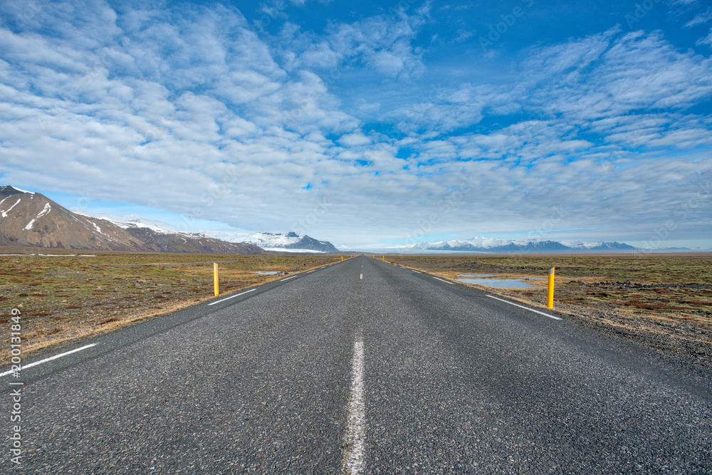 Endlessly straight road leading towards glacier and mountains at sunny day with blue half cloudy sky in Iceland