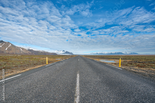 Endlessly straight road leading towards glacier and mountains at sunny day with blue half cloudy sky in Iceland