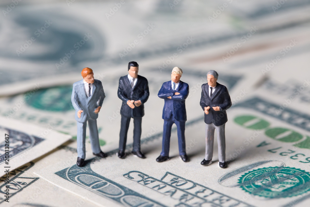 Miniature figurine toys standing on dollar with money and work concept. Focus on the businessman. Miniature figurine toys standing on dollar with money and work concept. Focus on the businessman.