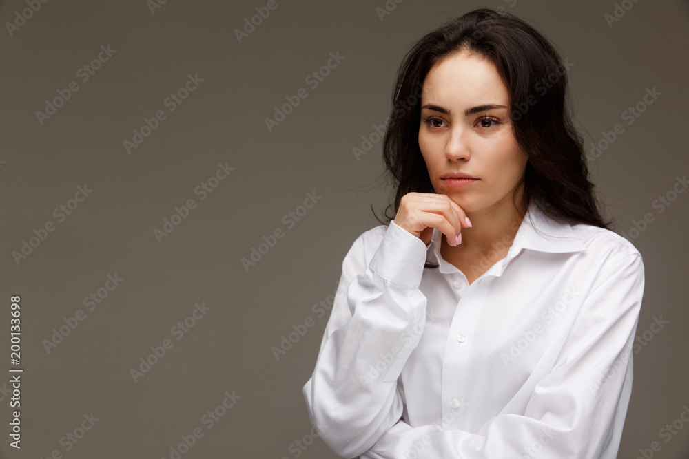 Beautiful girl in a white shirt shows emotions - thoughtfulness. On a light background. Beautiful girl in a white shirt shows emotions - thoughtfulness. On a light background.
