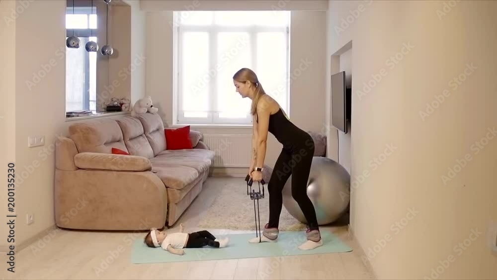 woman is engaged in sports in her apartment with a child who lies on the floor woman is engaged in sports in her apartment with a child who lies on the floor