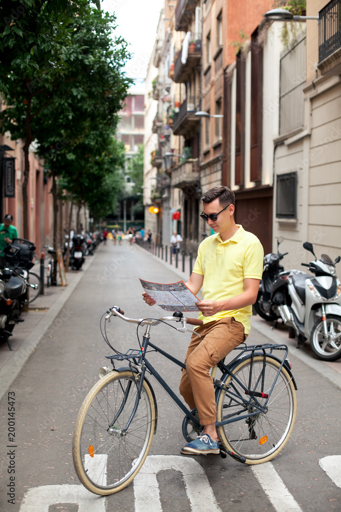 Hipster man riding vintage bike and reading map in tourist area in european city