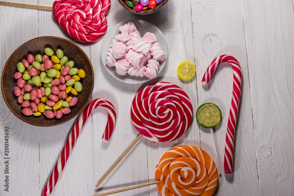 Colorful chocolate candies, lollipops, candy cane and marshmallows on wooden table