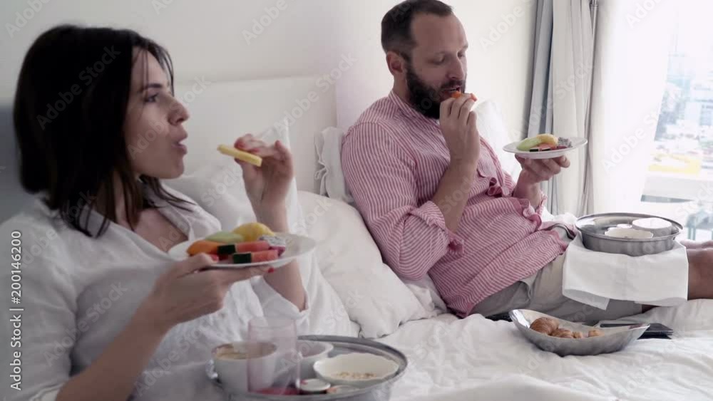 Young couple eating and talking during breakfast at bed
Young couple eating and talking during breakfast at bed