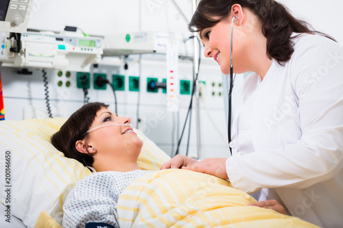 woman doctor at intensive care unit of clinic checking her patient with stethoscope