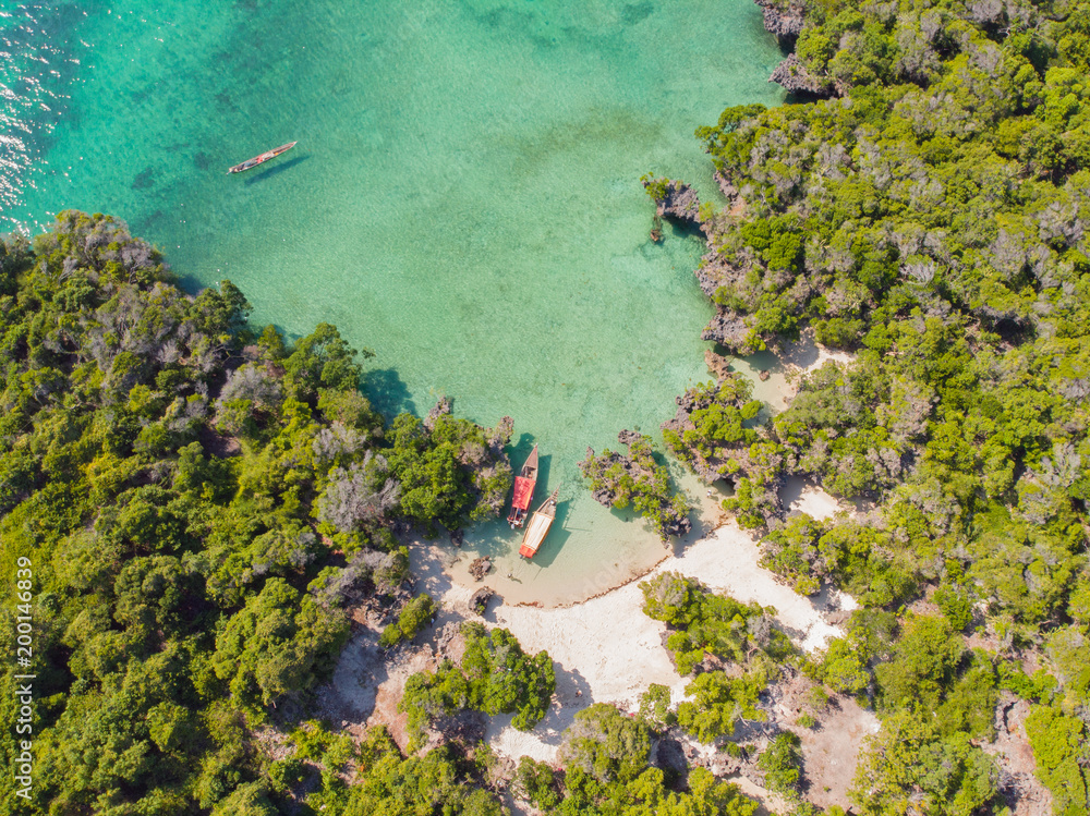 Aerial view of a beautiful tropical island and beach, small fisherman boat on clear blue reef water along Africa, Tanzania, Zanzibar. Indian Ocean