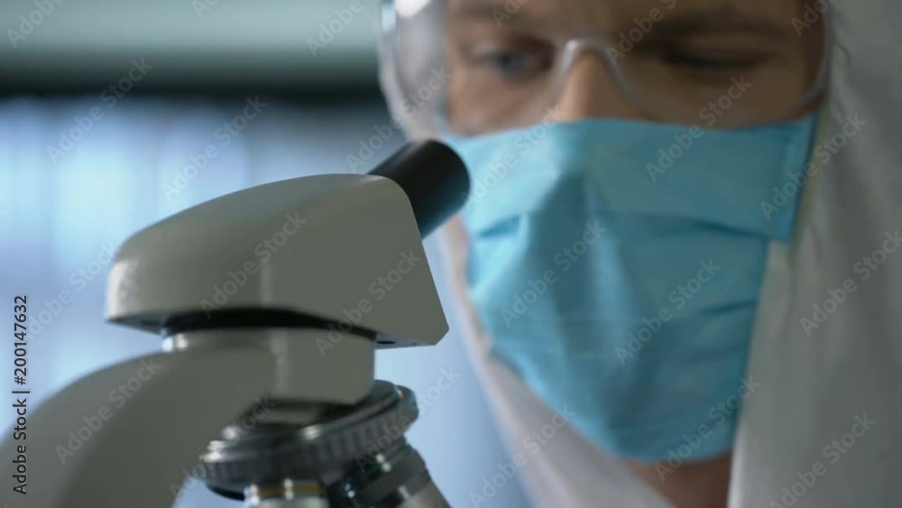 Lab assistant looking at microscope slide with blood, genetic research, closeup Lab assistant looking at microscope slide with blood, genetic research, closeup