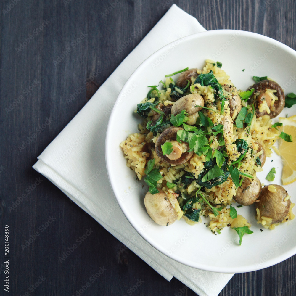 Vegetarian turmeric rice in the white bowl. Vegan dish. European cuisine. Yellow rice with mushrooms and spinach. Meatless. Toned photo. Top view. Vegetarian turmeric rice in the white bowl. Vegan dish. European cuisine. Yellow rice with mushrooms and spinach. Meatless. Toned photo. Top view.