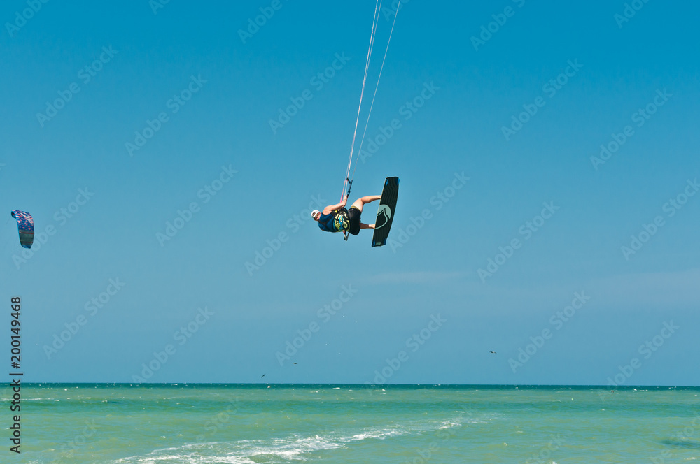 Fototapeta premium Front view of a young male, lifting out of water and spinning while kiteboarding at fast speed through rough ,tropical water of the Gulf of Mexico