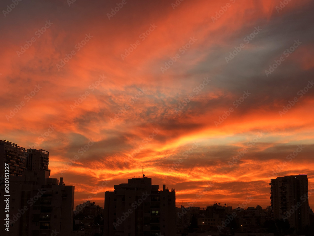 Sunset in the city with stunning colorful magic clouds. Spring sky with red clouds and roofs view.