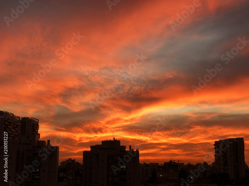 Sunset in the city with stunning colorful magic clouds. Spring sky with red clouds and roofs view.
