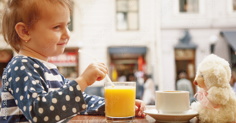 Little beautiful child girl drinking orange juices opposite of teddy bear with coffee. (Health, drink, thirst, childhood, carelessness concept) Little beautiful child girl drinking orange juices opposite of teddy bear with coffee. (Health, drink, thirst, childhood, carelessness concept)