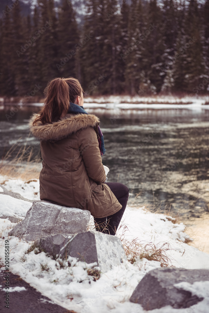 Woman sitting on river bank in winter Woman sitting on river bank in winter