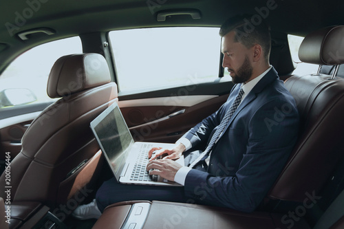 businessman using a laptop in the backseat of a car © ASDF