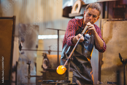 Glassblower shaping a glass on the blowpipe photo