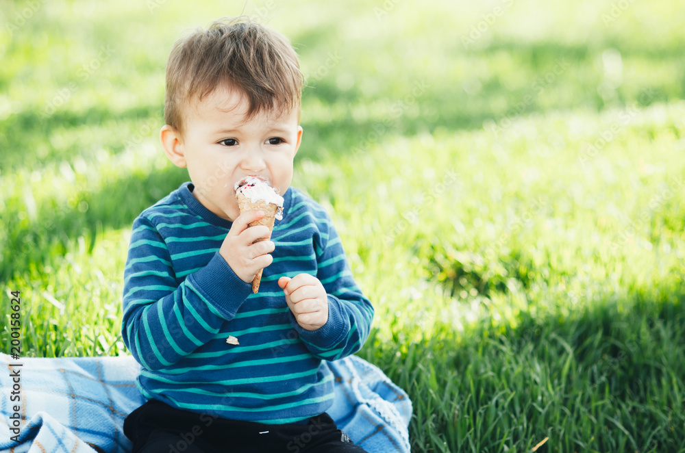 Cheerful child in a blue sweater eating ice cream on a background of grass, outdoors Cheerful child in a blue sweater eating ice cream on a background of grass, outdoors