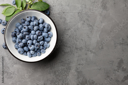 Fresh ripe blueberries with leaves in bowl on gray stone background, top view