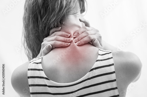 Woman with upper back and neck pain standing with her back to the camera and her hand rubbing her shoulder muscles close to the spine photo