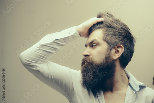 Barbershop or hairdresser concept. Macho on strict face, wears unbuttoned shirt. Man with long beard, mustache and stylish hair, light background. Guy with modern hairstyle visited hairdresser.