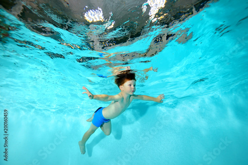 A little boy is engaged in underwater sports in the pool. Swims under water like a bird and looks forward. Portrait. Shooting underwater at the bottom. Horizontal view