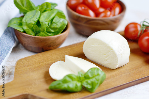Mozzarella cheese with red tomatoes and basil leaves, pepper, olive oil, wooden desk, healthy food concept