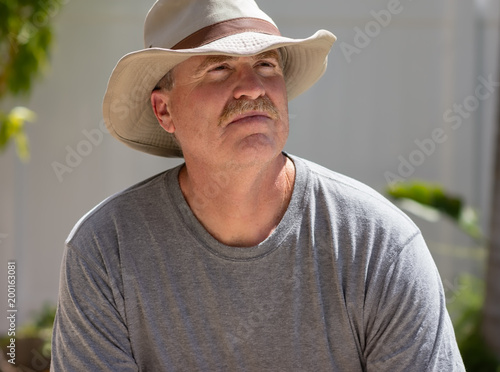Canvas-taulu Older male looks up into bright sun wearing wide brim hat