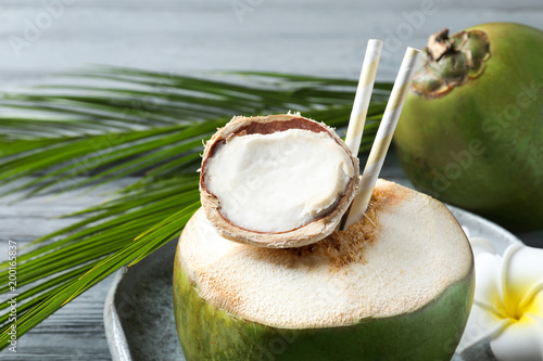 Fresh green coconut with drinking straws on table, closeup