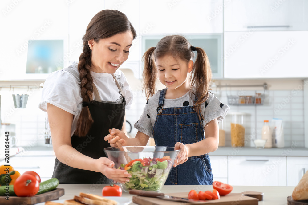 Young nanny with cute little girl cooking together in kitchen