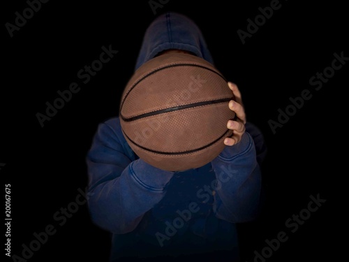 hooded basketball player holding ball in hands isolated in dark background © Mihail