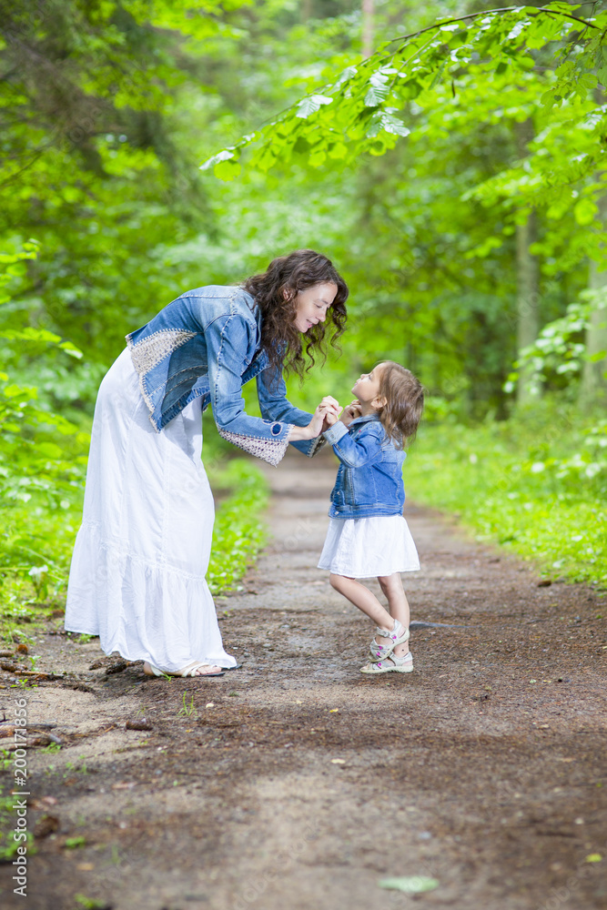 Family Ideas and Concepts. Happy Mother and Her Little Caucasian Daughter Posing with Playful Expression Together In Green Summer Forest. Family Ideas and Concepts. Happy Mother and Her Little Caucasian Daughter Posing with Playful Expression Together In Green Summer Forest.