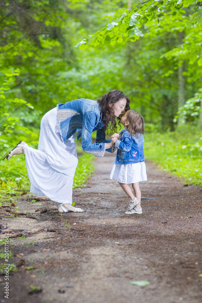 Fototapeta premium Family Ideas and Concepts. Happy Mother and Her Little Caucasian Daughter Posing with Kissing Expression Together In Green Summer Forest.