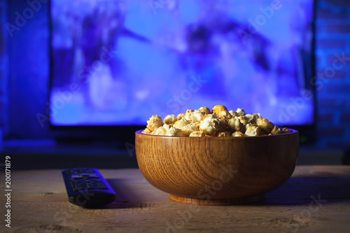 Foto A wooden bowl of popcorn and remote control in the background the TV works