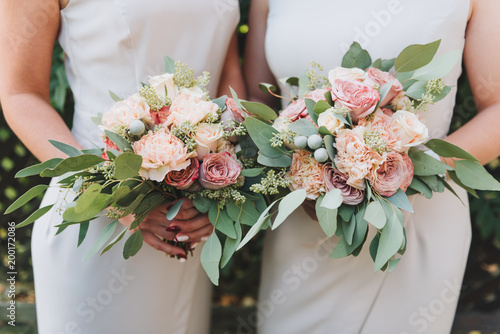 Two bridesmaids wearing white dresses holding their bouquets with peonies and eucalyptus