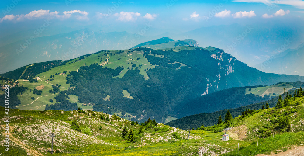 Panoramic view landscape in Dolomite Alps, Italy, with fresh green meadows and blooming flowers and mountain tops in the background.Panorama of Monte Baldo, European Alps on a sunny day with blue sky