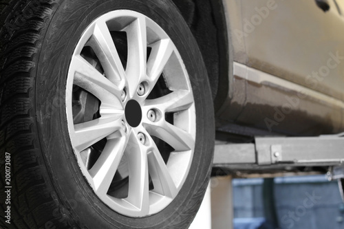 Car on hydraulic vehicle lift in garage, closeup. Tire service