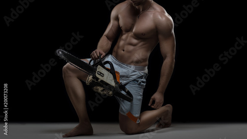 Worker concept. Young muscular shirtless man in denim uniform with chainsaw