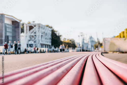 Multiple red plastic insulated tubes with electrical cables inside are laying on the asphalt of a city construction zone ready for laying underground; shallow depth of field, silhouettes of people