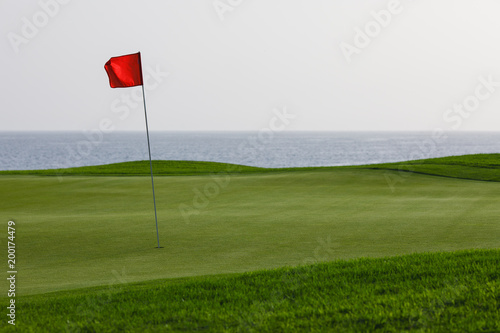 golf course with green grass and red pin flag, sea background