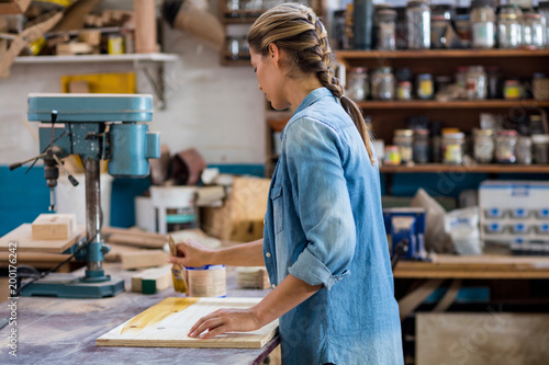 Female carpenter applying varnish on wooden plank photo