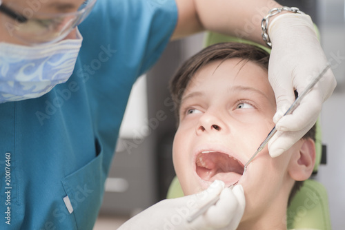 Boy with perfect teeth at the dentist doing check up while other doctors analyze x-ray in the background - oral hygiene health care concept