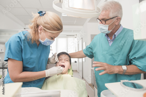 Boy with perfect teeth at the dentist doing check up with two doctors - oral hygiene health care concept