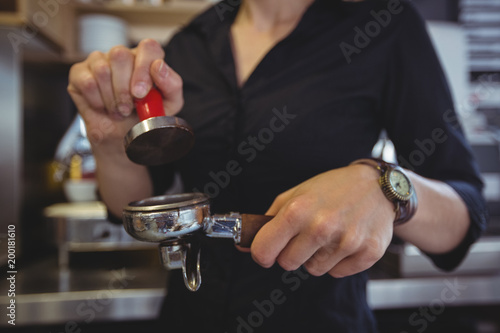 Close-up of waitress using a tamper to press ground coffee into a portafilter
