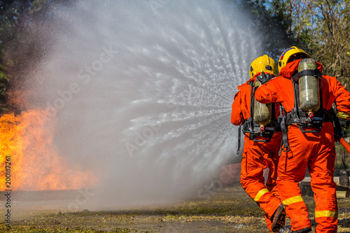 Firefighter using extinguisher and water from hose for fire fighting, Firefighter spraying high pressure water to fire with copy space.