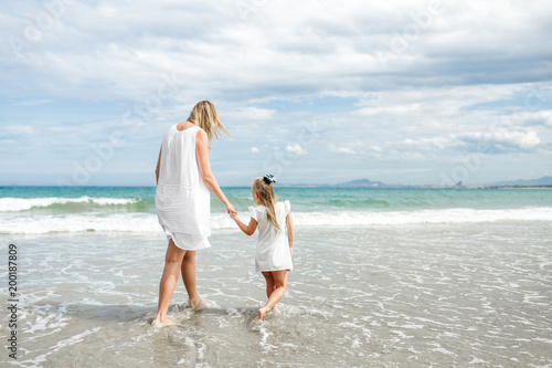Back view family mother and daughter walking at beach enjoying tropical summer vacation.