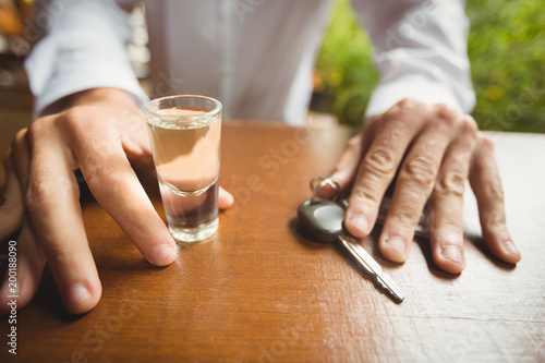 Man holding glass of tequila shot and car key in bar counter photo