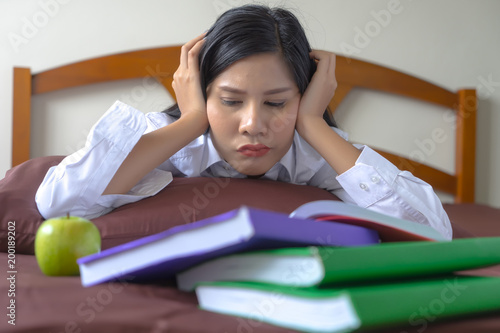 Young Asian woman reading books on bed feeling upset. Serious girl feeling bad, nervious about exam. photo